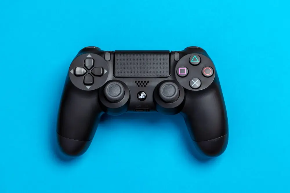 Flat lay photo of black sony ps4 game controller on blue background